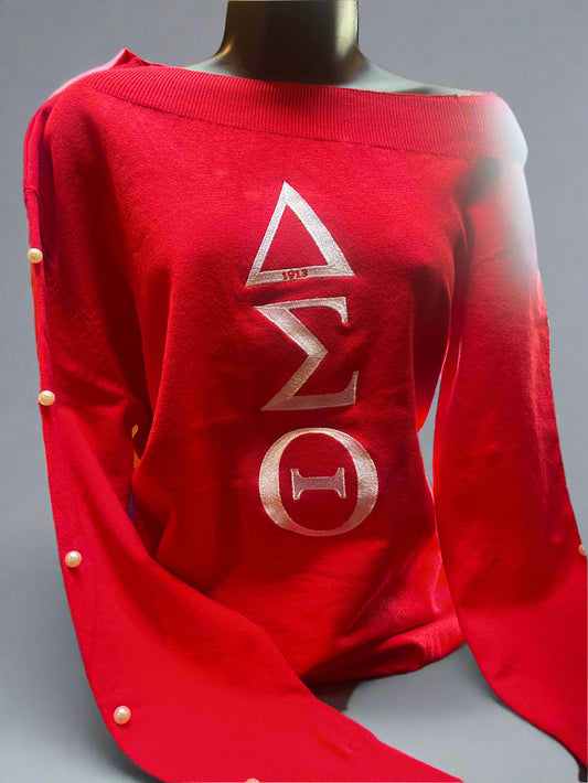 A Little Pearled Off The Shoulder is a bold red sweater with a feminine off-shoulder fit. Pearl detailing along the sleeves adds a polished Delta touch. A chic and stylish piece for any DST event or outing.