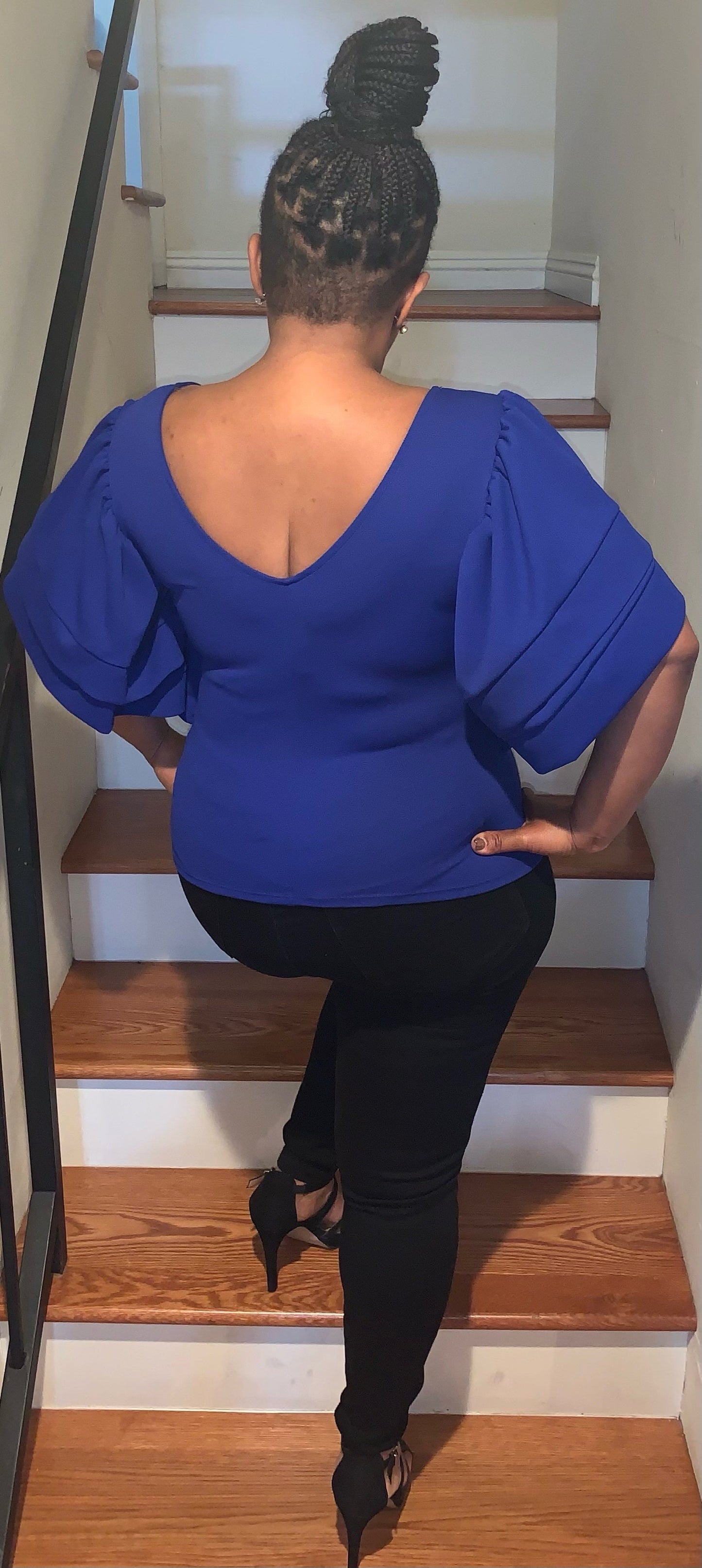 A woman wearing a royal blue blouse with ruffles, featuring the text 'Finer Since 1920' on the front. Back view