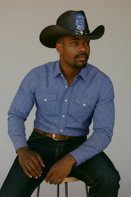 Man wearing a blue patterned shirt and phi beta sigma black cowboy hat with a logo indoors.